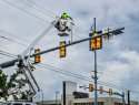 An electrician fixes a high-voltage transmission line above a traffic light.