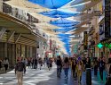 People walk on a busy urban shopping street covered with shade sails.