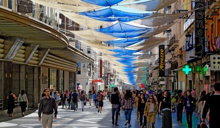 People walk on a busy urban shopping street covered with shade sails.