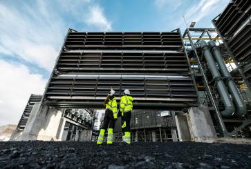 Two people wearing safety jackets look up at the Mammoth Direct Air Capture plant.