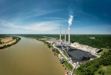Aerial view of a power plant on a river with piles of coal and smoke rising from smokestacks.