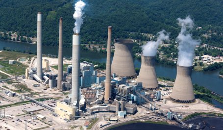 Aerial view of smoke coming from a coal-fired power plant on the banks of a river.