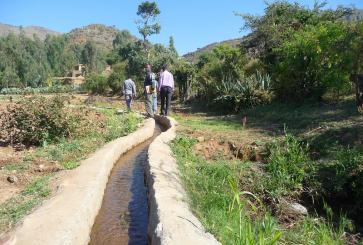 People walking along irrigation channel with greenery along its edges.