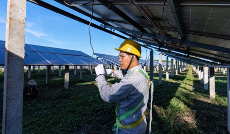 A worker connecting electrical cords beneath a solar panel.