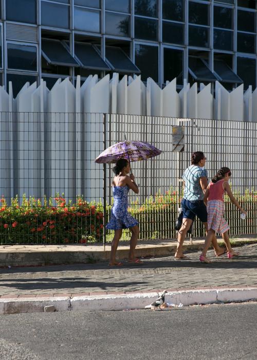 People walking on sidewalk holding umbrellas on a sunny day.