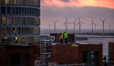 Construction workers on a rooftop with wind turbines. 