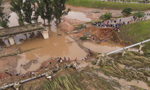 Commuters stuck at a flooded river with a damaged bridge.