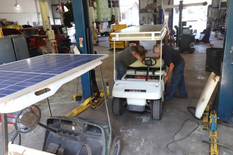 Two people install electric solar battery in a golf cart.