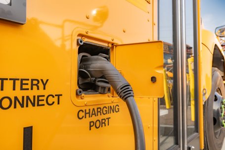 A yellow electric school bus plugged into a charging station.