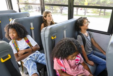 Four students sit in two rows of two inside an electric school bus.