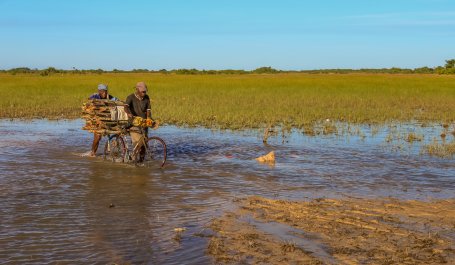 Two villagers in Mozambique push a bicycle through a flooded street.