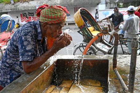 A man drinks from an outdoor water tap in the city.