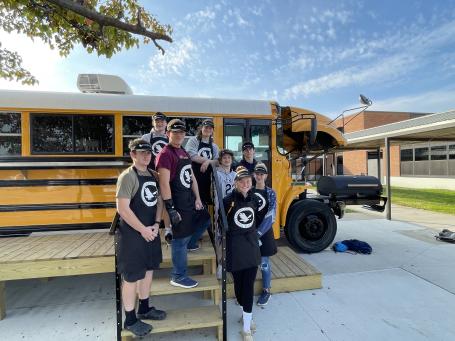A group of students standing outside of a school bus converted into a coffee shop.