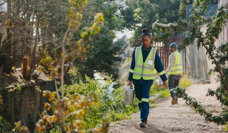 Two workers tend to plants on a riverbank.