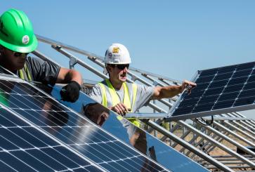 Three people installing a solar panel. 