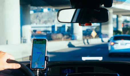 A driver following GPS directions on a mounted smartphone, taken from the backseat of the car.