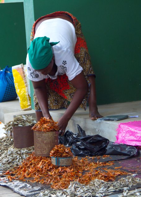 A woman bends over to reach for shrimp at a market.