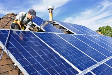 A construction worker secures new solar panels to a residential roof.