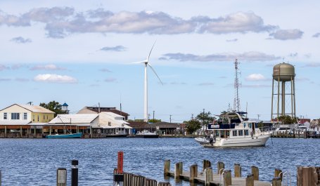 A wind turbine is seen across the water near homes.