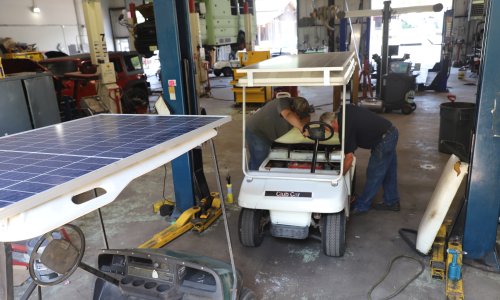 An instructor and student in an automotive garage working on a solar-powered golf cart.