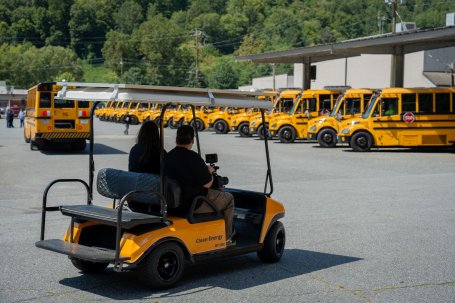 Two people driving a solar-powered electric golf cart in a parking lot.