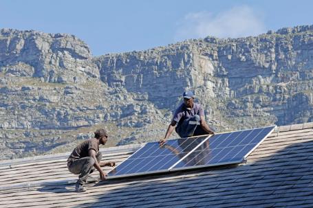 Two technicians install solar panels on a rooftop.