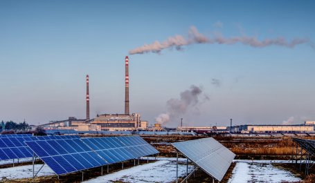 Solar panels with smoke from a smokestack in the background.