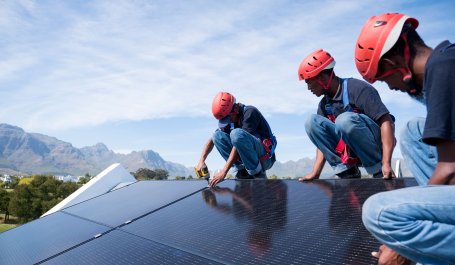 Three workers installing solar panels on a roof.