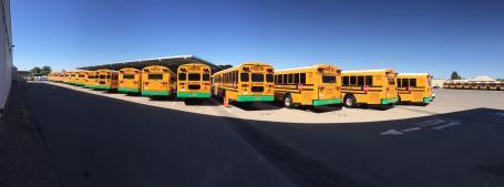 A fleet of electric busses sitting in a large lot.