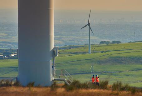 Two neon-vested workers exit a wind turbine.
