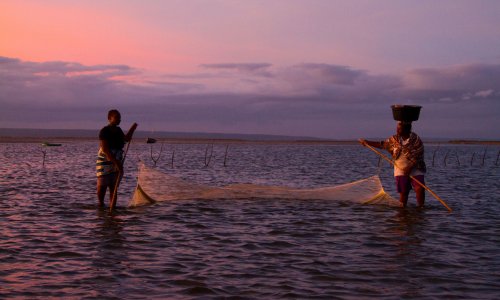 Two women hold a guínia net while standing in Inhambane Bay at sunrise. 